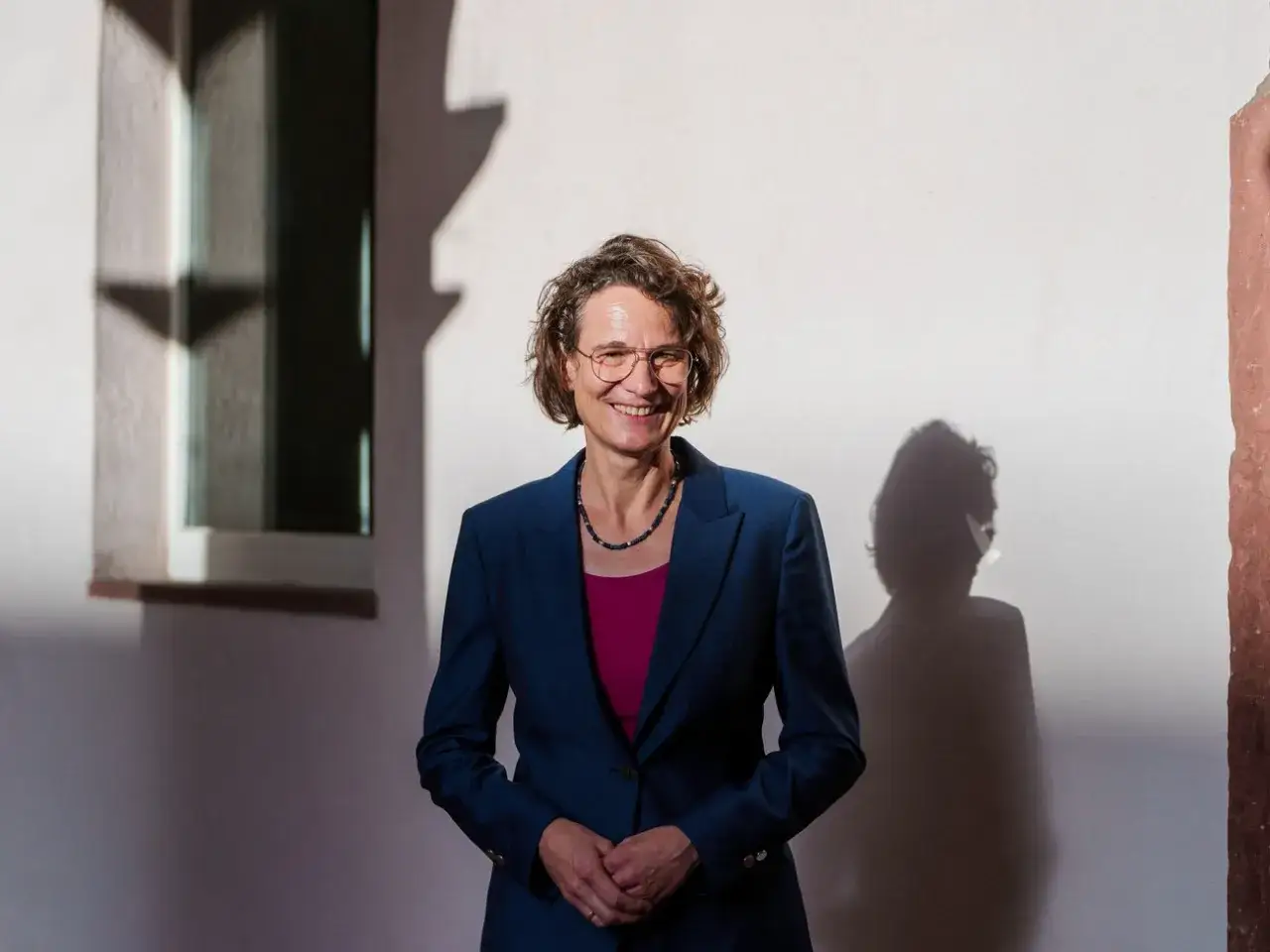 Christiane Tietz l&auml;chelt in die Kamera, gekleidet in einen blauen Anzug. Ihr Schatten wirft sich an die Wand.