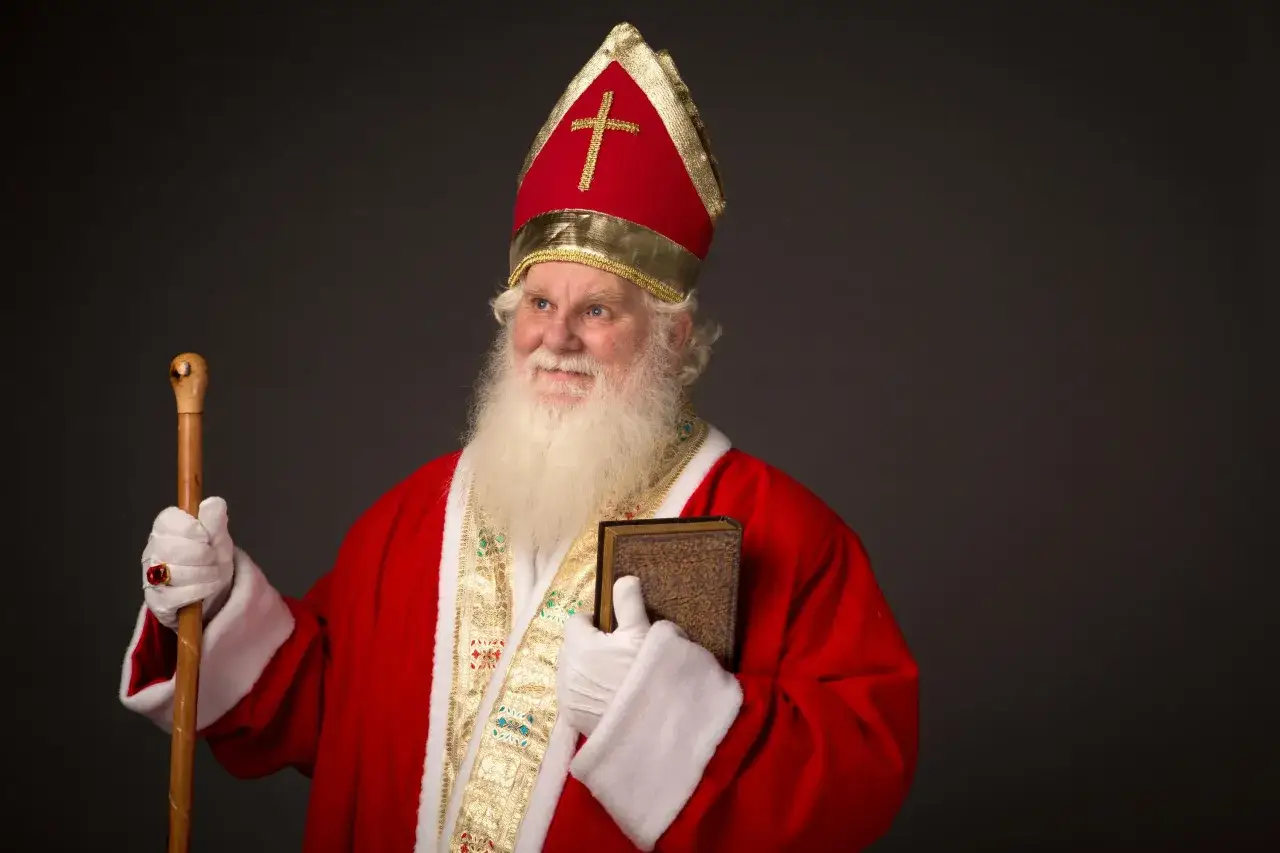Ein Mann im Bischofsornat mit Mitra und Stab, der ein Buch hält. Er erinnert an die Legende von Nikolaus von Myra, der für seine Großzügigkeit bekannt war.