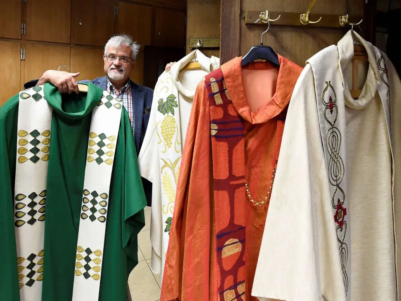 Mann präsentiert liturgische Gewänder in verschiedenen Farben, darunter ein grünes Gewand in der Farbe Kardinal.