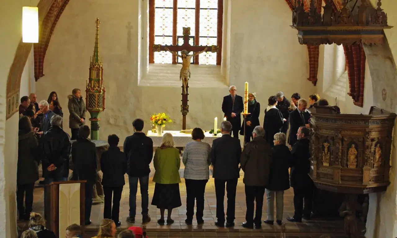 Menschen stehen in einer Kirche vor einem Kreuz. Eine Frau in Gr&uuml;n steht vorn. Kommt, sagt es allen weiter.