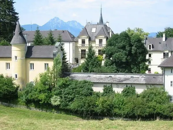 Gelbes Gebäude mit Türmchen und Bergkulisse, erinnert an ein Kloster in Salzburg.