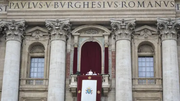 Der Papst steht auf dem Balkon des Petersdoms, umgeben von Kardinälen. Ein großes Wappen hängt über dem Balkon.